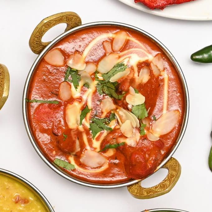 Butter chicken curry with cream drizzle and almonds in a brass karahi