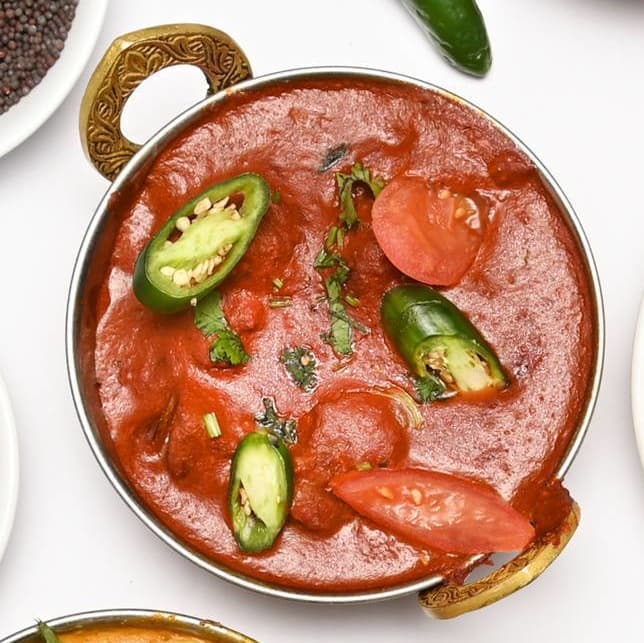 Tomato-based curry garnished with green chillies and fresh herbs