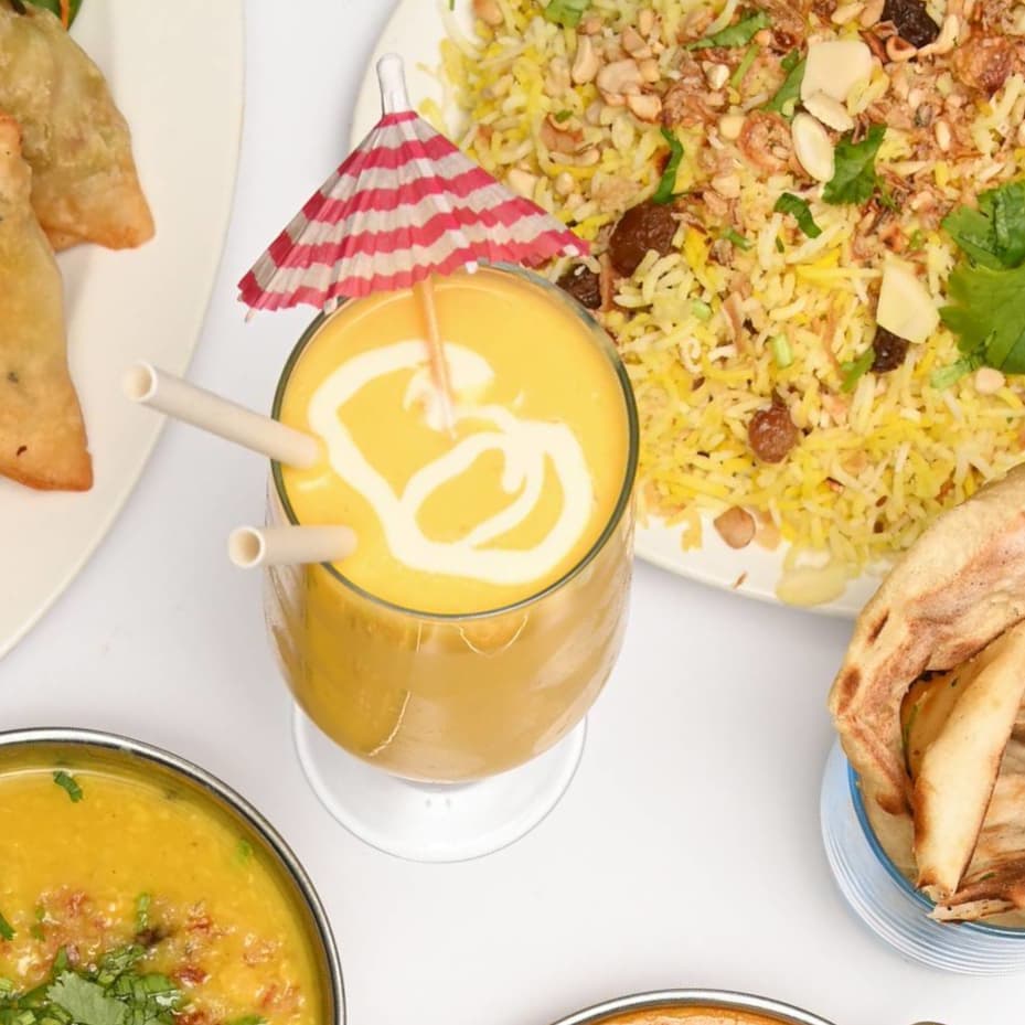 Mango lassi with biryani, samosas, daal, and naan spread